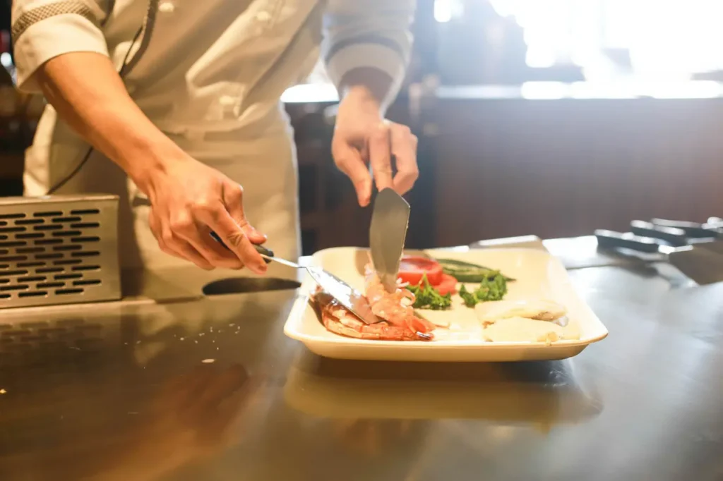 Chef preparing a seafood dish with fresh vegetables on a white plate.